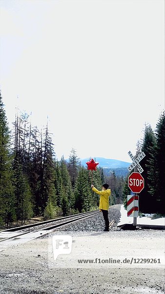 Frau hält roten Sternballon an Eisenbahnschienen