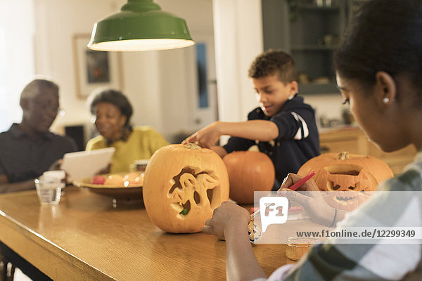 Grandparents at table with grandchildren carving Halloween pumpkins