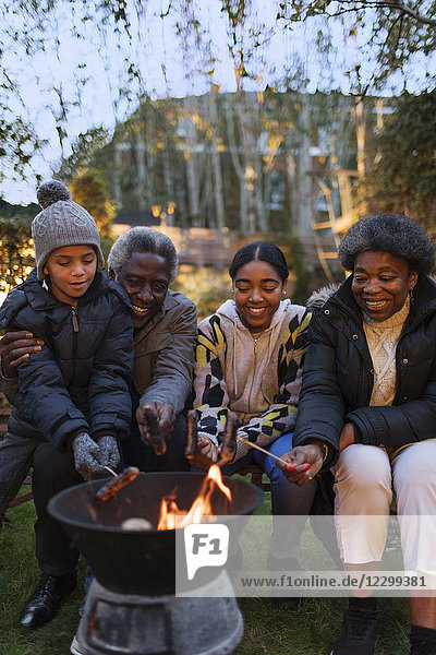 Grandparents and grandchildren roasting hot dogs over campfire