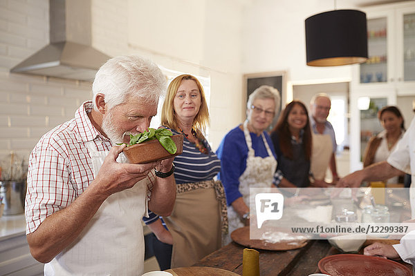 Active senior friends taking cooking class  smelling fresh basil