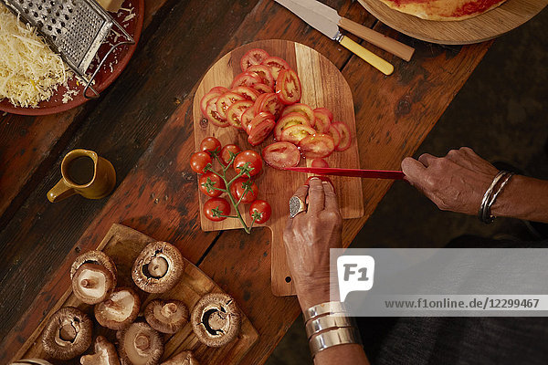 Overhead view woman slicing fresh tomatoes for pizza