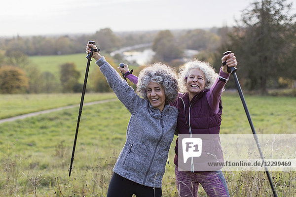 Portrait enthusiastic  confident active senior women friends hiking with poles in rural field