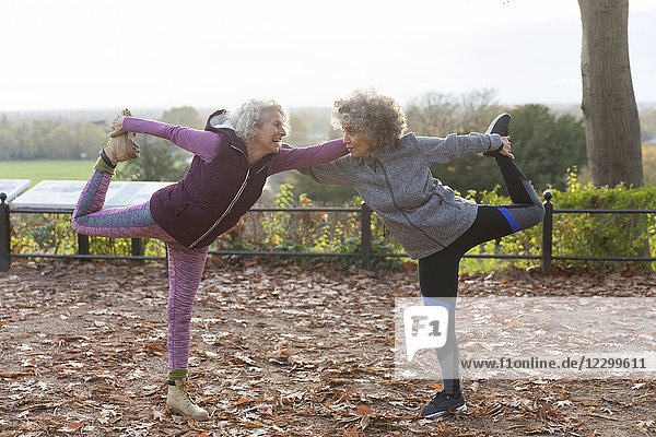 Active senior women friends stretching in autumn park