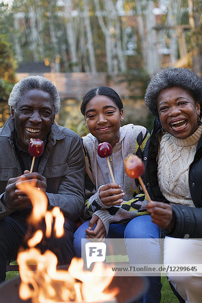 Portrait smiling  happy grandparents and granddaughter enjoying candy apples at campfire