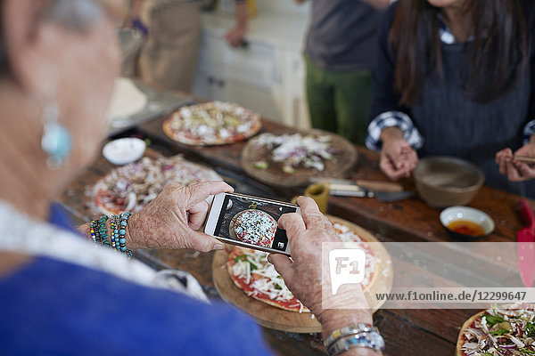 Senior woman with camera phone photographing homemade pizza in cooking class