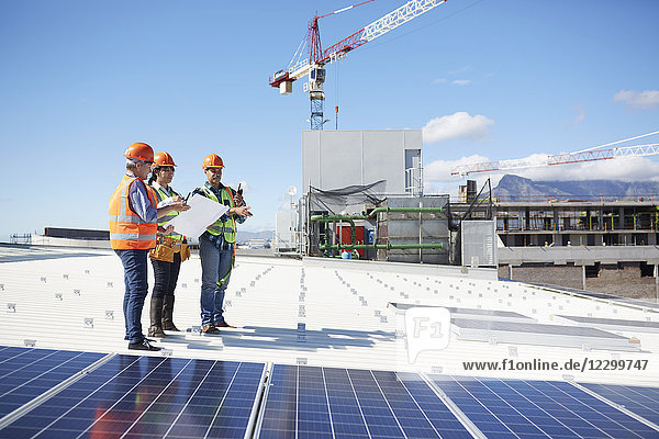 Engineers with blueprint at solar panels at sunny power plant