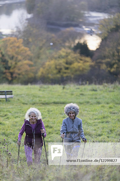 Active senior women friends hiking with poles up rural hillside