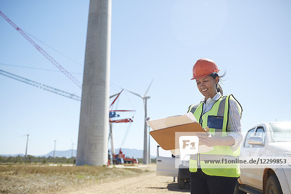 Smiling female engineer with blueprint at sunny wind turbine power plant