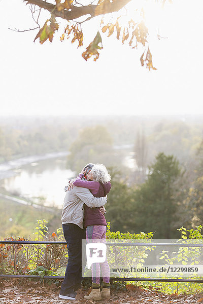 Affectionate active senior couple hugging in sunny autumn park
