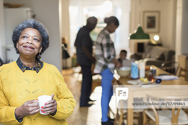 Smiling  satisfied senior woman drinking coffee with family in background