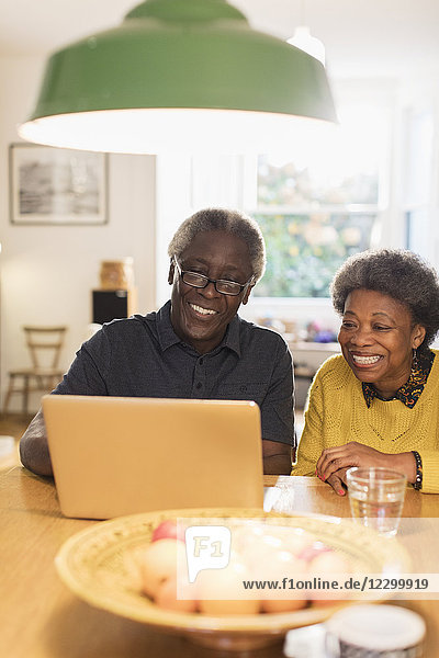 Happy senior couple using laptop in kitchen