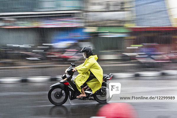 Side view of person in raincoat riding motorcycle during rain in street of Jakarta  Indonesia
