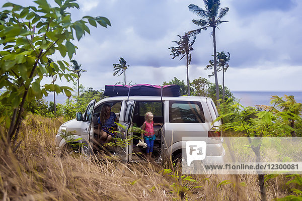 Frau mit Mädchen im Auto am Meeresufer in tropischer Landschaft mit Palmen  Nusa Penida  Bali  Indonesien