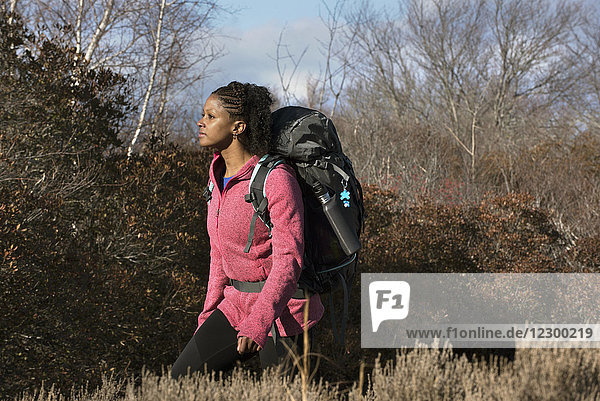 Young woman hiking with backpack in front of various bushes  Newburyport  Massachusetts  USA