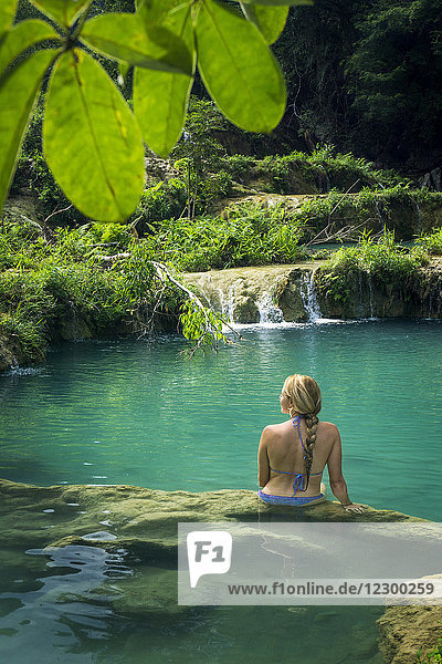 Rückansicht einer Frau im Bikini  die im Fluss sitzt  mit Blick auf einen Wasserfall  Semuc Champey  Guatemala