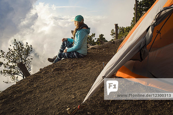 Side view of young female hiker sitting outside tent at summit of Acatenango Volcano  Guatemala