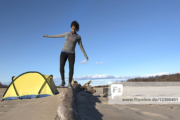 Junge Frau balanciert auf Treibholz  das in der Nähe eines Campingplatzes am Küstenstrand liegt  Newburyport  Massachusetts  USA