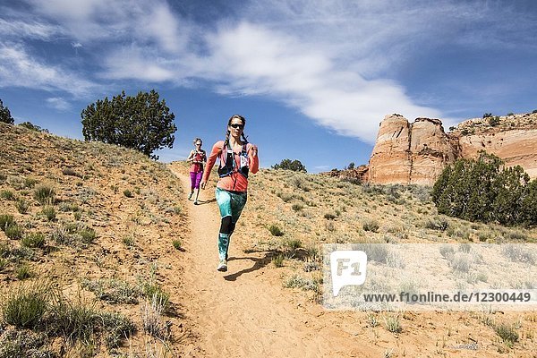 Front view of two women trail running down hill through desert in Grand Staircase-Escalante National Monument  Utah  USA