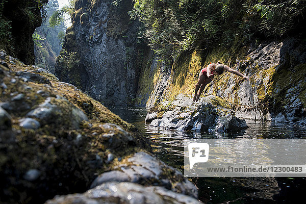 Frau im Bikini taucht von einem Felsen ins Wasser