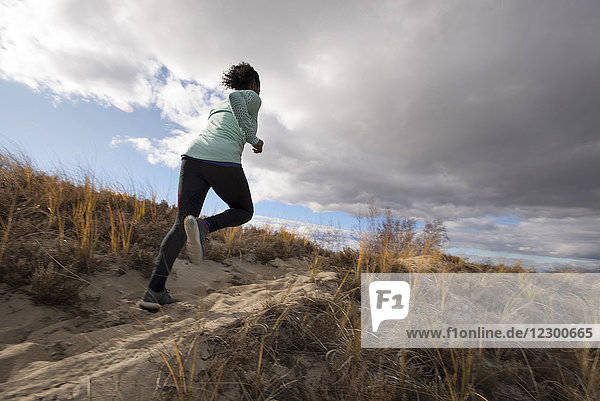 Rear view of young woman jogging on sand against large clouds  Newburyport  Massachusetts  USA