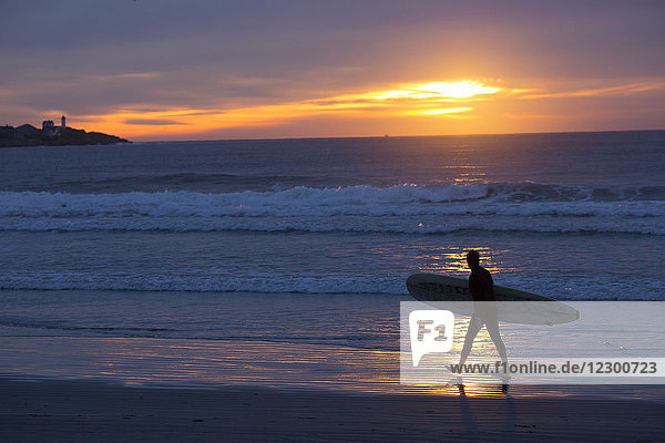 Surfer mit Surfbrett am Strand bei Sonnenaufgang  Long Sands Beach  York  Maine  USA