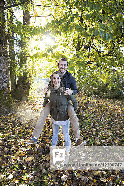 Front view of couple in park with woman giving man piggyback ride