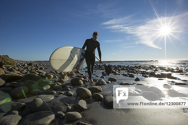 Man carrying stand up paddleboard on rocky beach