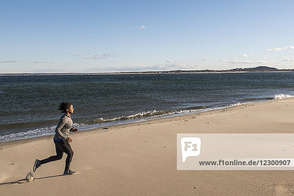Young woman jogging on sandy beach along ocean coastline  Newburyport  Massachusetts  USA