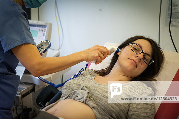 Reportage in der Notaufnahme für Entbindungen  Gynäkologie und Geburtshilfe im Krankenhaus Métropole  Chambéry  Frankreich. Eine Hebamme misst die Temperatur einer Frau  die in der 40. Woche schwanger ist und die Bewegungen ihres Babys nicht mehr so stark spürt wie am Vortag.