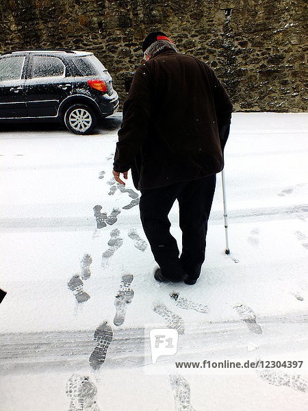 An elderly man walking in the snow.