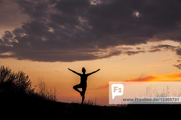Silhouette of woman doing yoga at sunset  standing on one leg and holding arms in the air