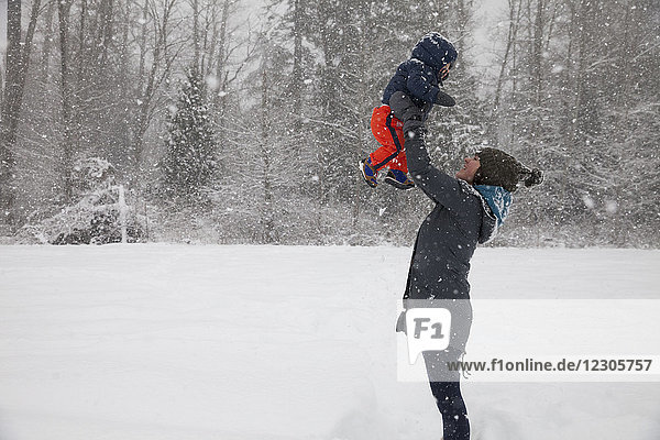 Mutter hält ihren kleinen Sohn beim Spielen im Freien im Winter hoch