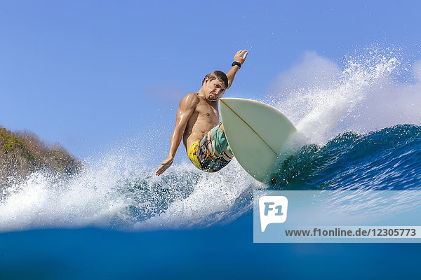 Junger Mann reitet auf einem Surfbrett auf einer Welle im Meer