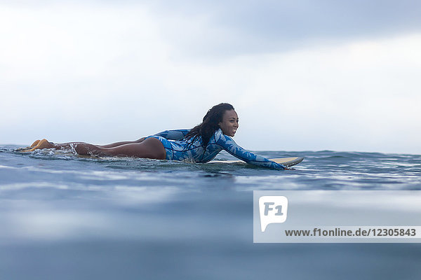 Seitenansicht einer Frau  die auf einem Surfbrett im Meer paddelt