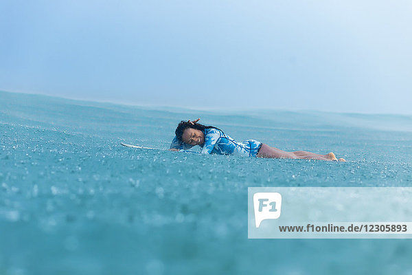 Lächelnde Frau auf Surfbrett im Meer liegend