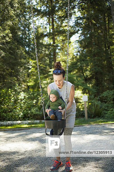 Vorderansicht einer Mutter mit ihrem kleinen Sohn  der auf einer Schaukel im Park spielt