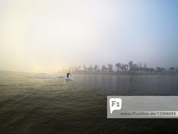 Surfer reitet Welle bei nebligem Wetter unter klarem Himmel bei Sonnenaufgang