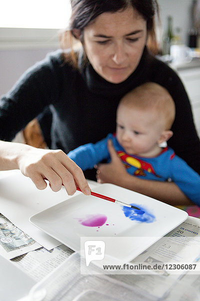 Mother helping baby paint art dripping paint on paper Kerroch Brittany France