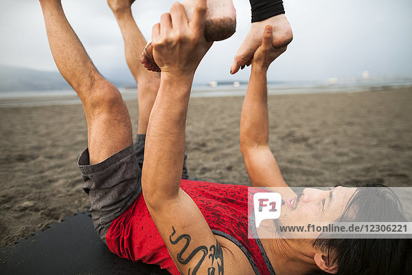 Mann hält Frau in der Luft und balanciert beim Acroyoga am Strand