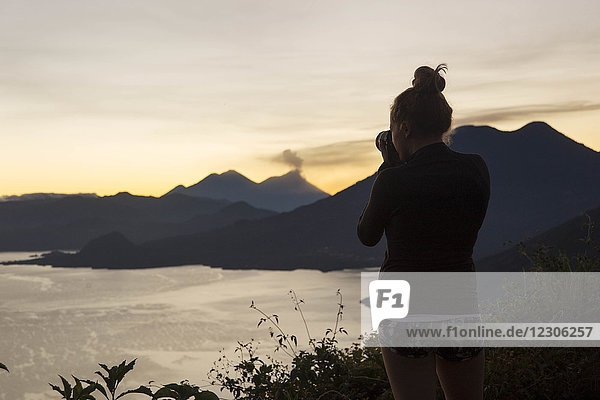 Rückansicht einer Frau  die den Sonnenaufgang am Atitlan-See  Guatemala  fotografiert