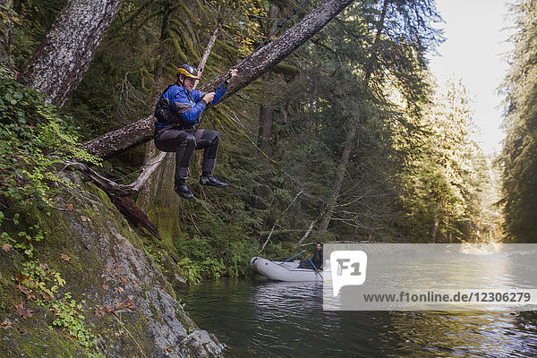 Side view of man on rope swing on riverbank in forest Opal Creek Wilderness Oregon USA