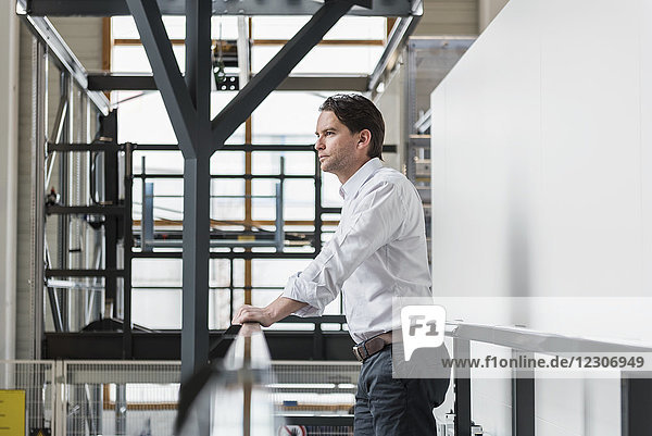 Businessman standing at railing in factory thinking