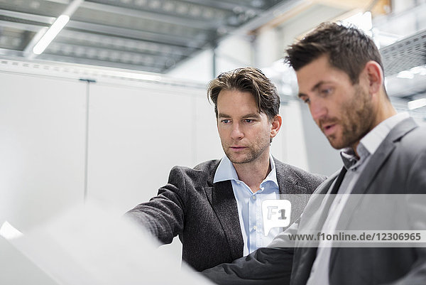 Two businessmen looking at plan in modern factory