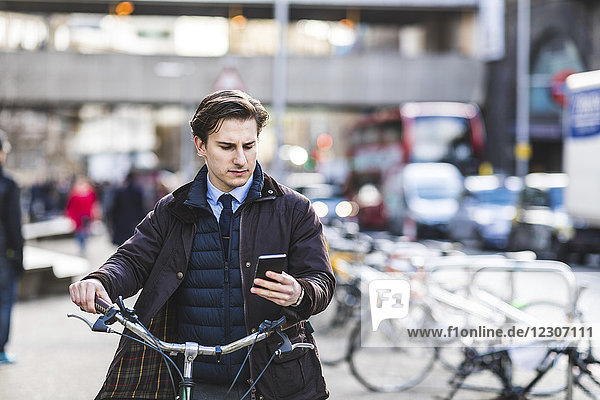 UK  London  businessman pushing bicycle in the city while looking at cell phone