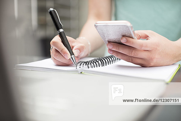 Frau schreibt Notizen im Tagebuch  hält ein Smartphone in der Hand
