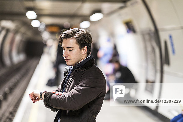 UK  London  Geschäftsmann  der an der U-Bahn-Station wartet und die Zeit überprüft.