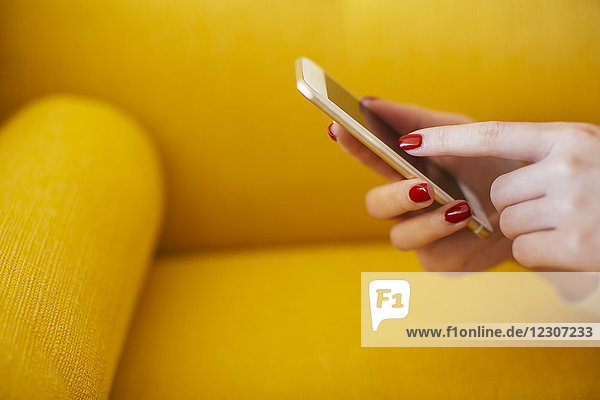 Frau mit Smartphone  gelbes Sofa