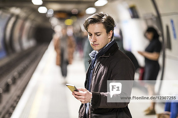 UK  London  Geschäftsmann wartet in der U-Bahn-Station mit Handy