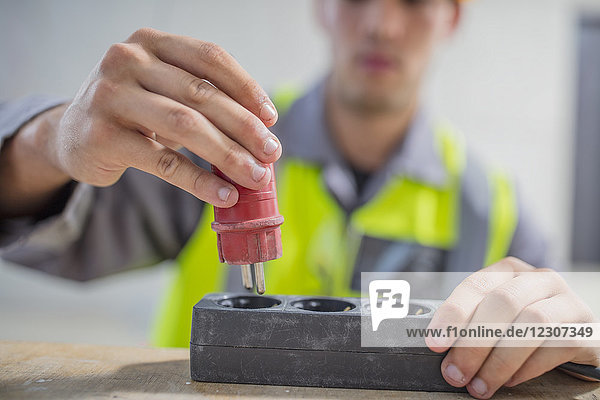 Close-up of electrician putting plug into power strip