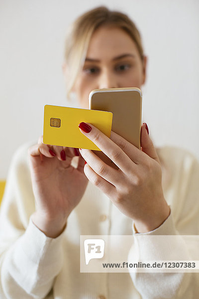Blonde Frau mit Smartphone und Bankkarte zu Hause